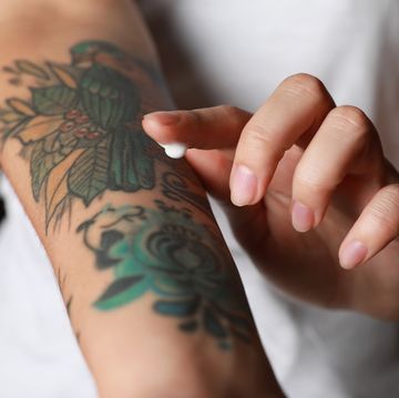 woman applying cream on her arm with tattoos against black background, closeup